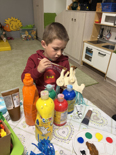 Chlapec barví u stolečku dřevěného koníka